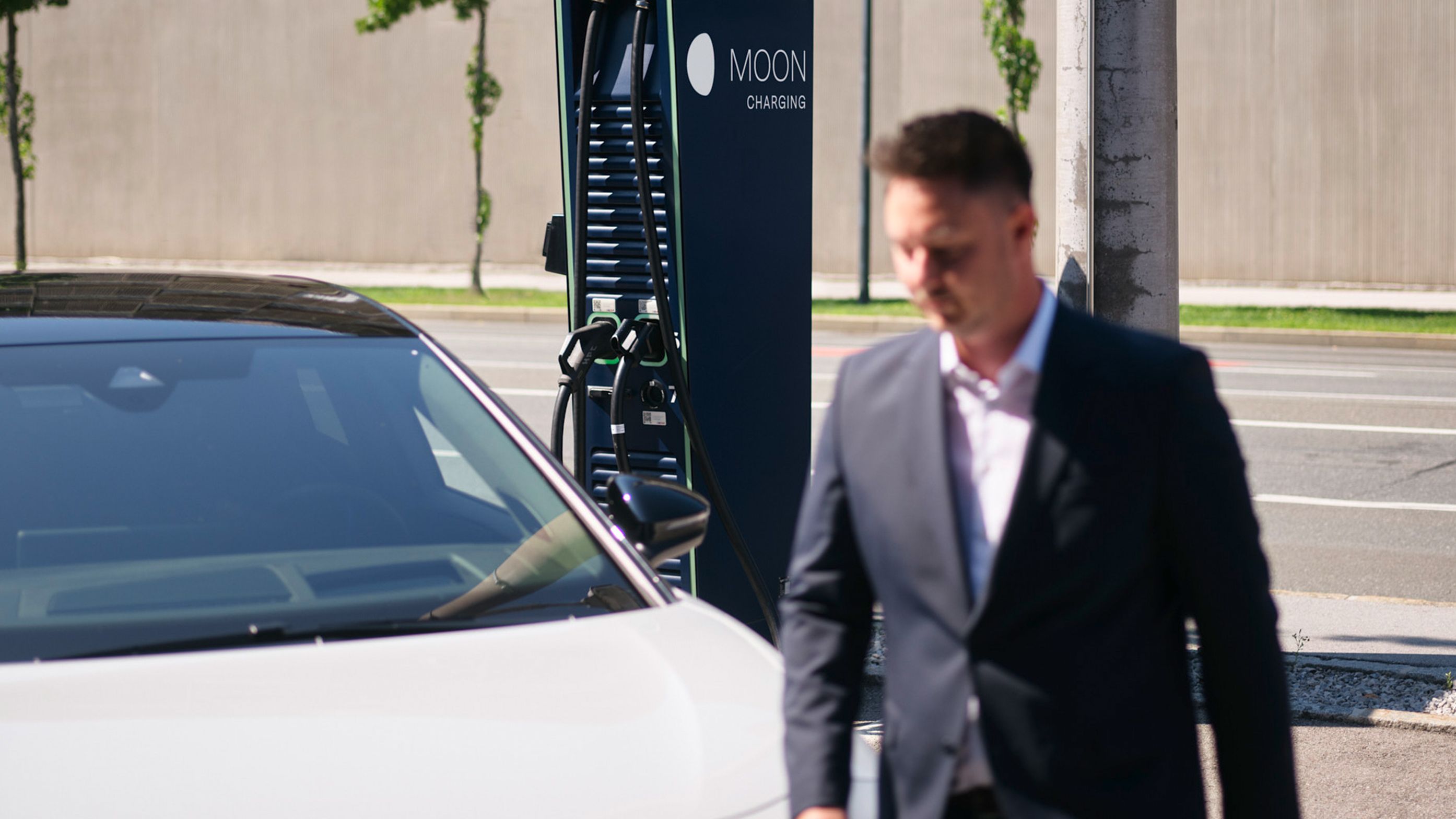 Man walks in front of a car in front of a charging station