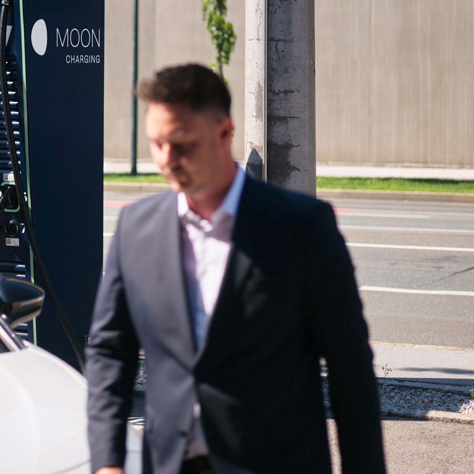 Man walks in front of a car in front of a charging station