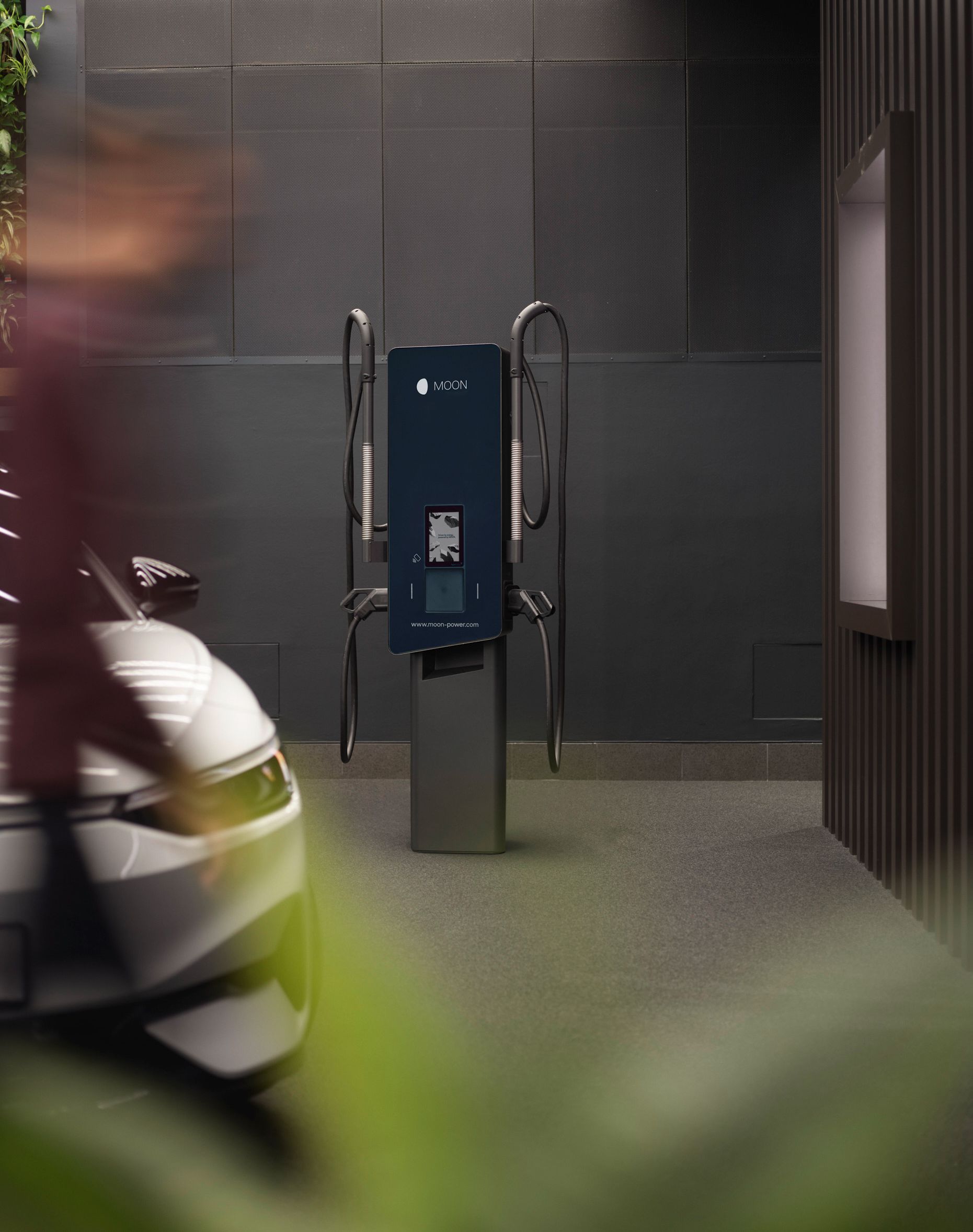 Wallbox in front of a gray wall with electric car in the foreground