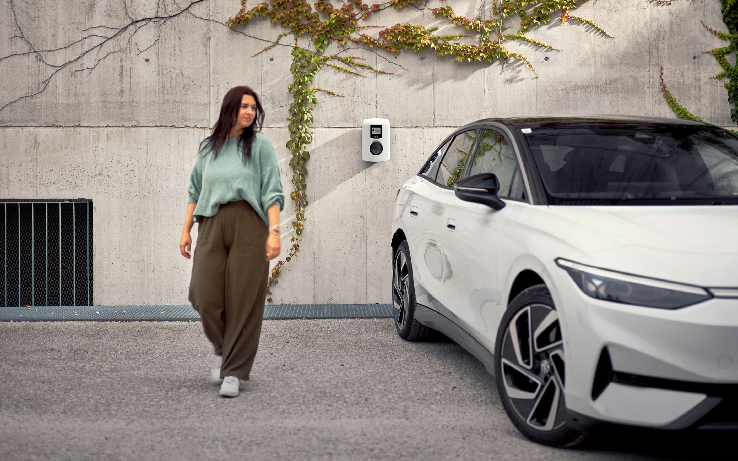 Woman walking next to a white car in front of a wallbox