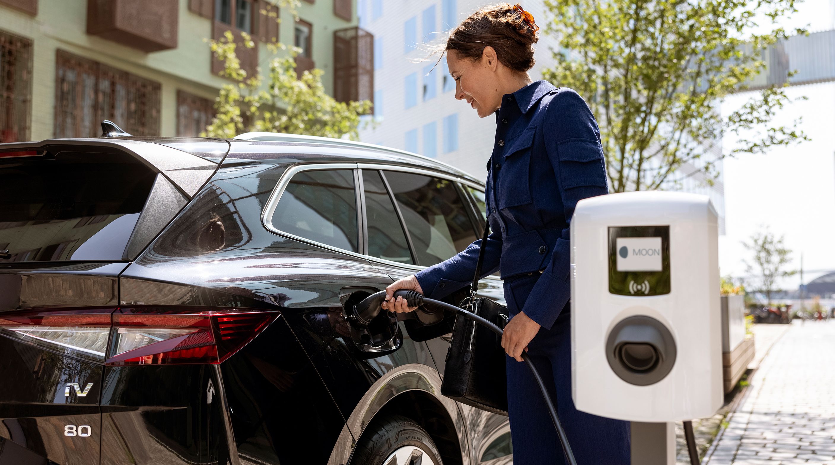 Woman inserting tap valve into an electric car with a wallbox in the foreground