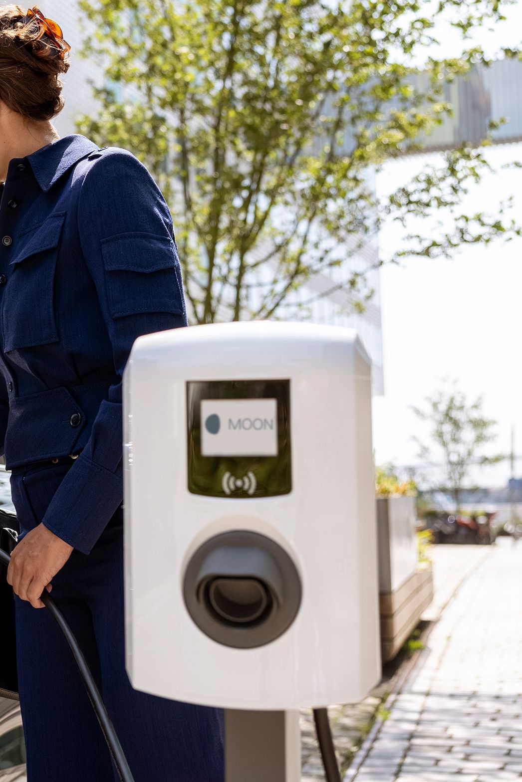 Woman inserting tap valve into an electric car with a wallbox in the foreground