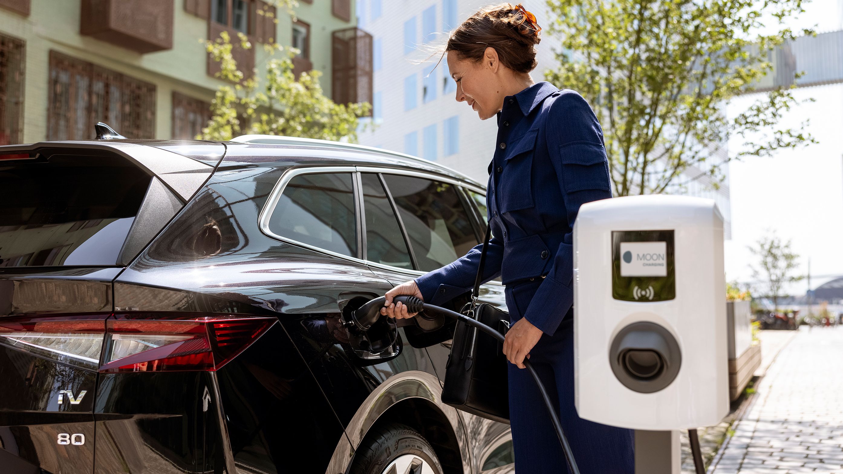 Woman inserting tap valve into a car with a wallbox in the foreground
