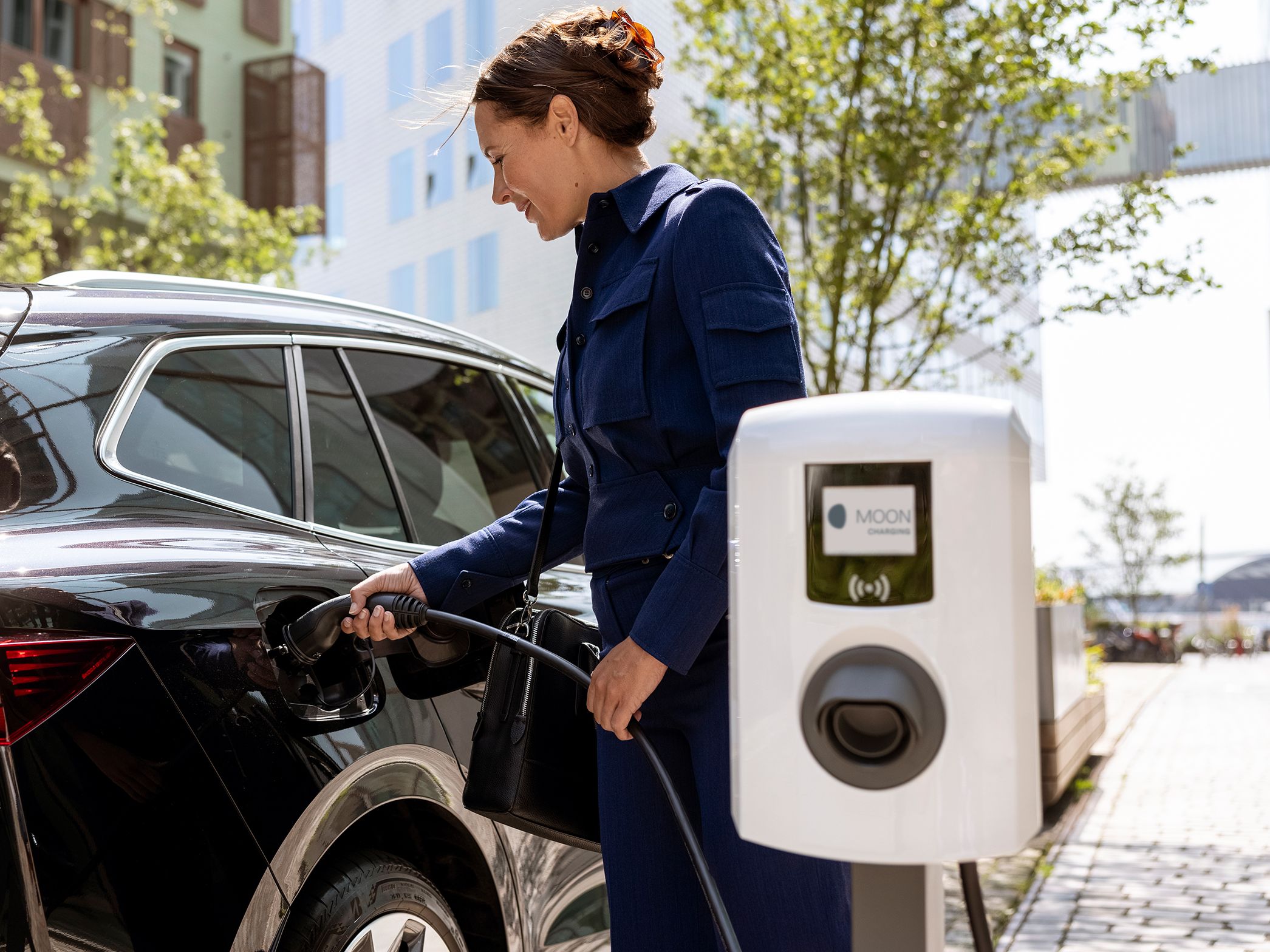 Woman inserting tap valve into a car with a wallbox in the foreground