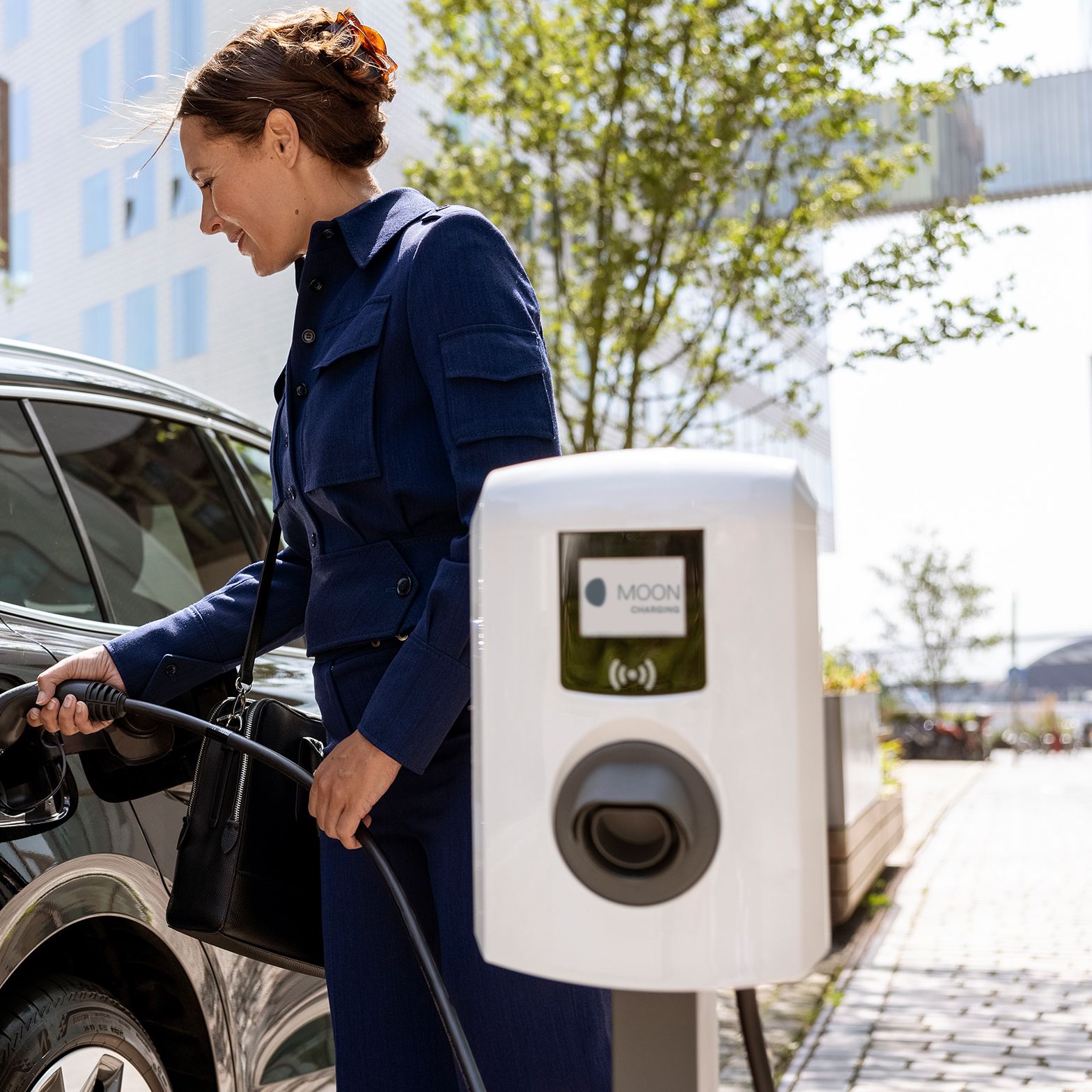 Woman inserting tap valve into a car with a wallbox in the foreground