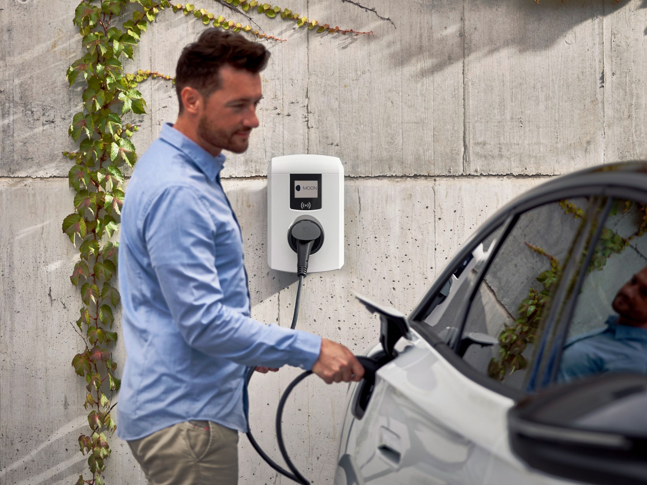 Man sticks tap valve of a wallbox into an electric car