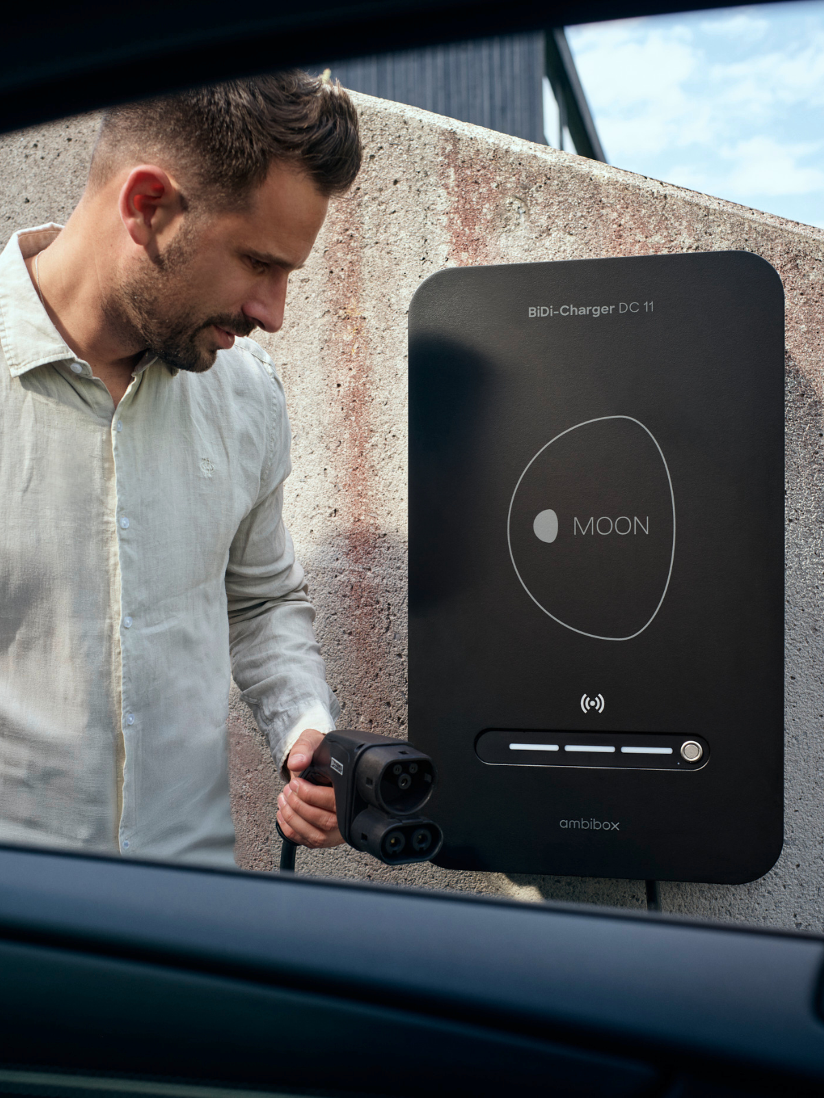 Mann mit bidirektionaler Wallbox MOON BiDi Charger vor Auto