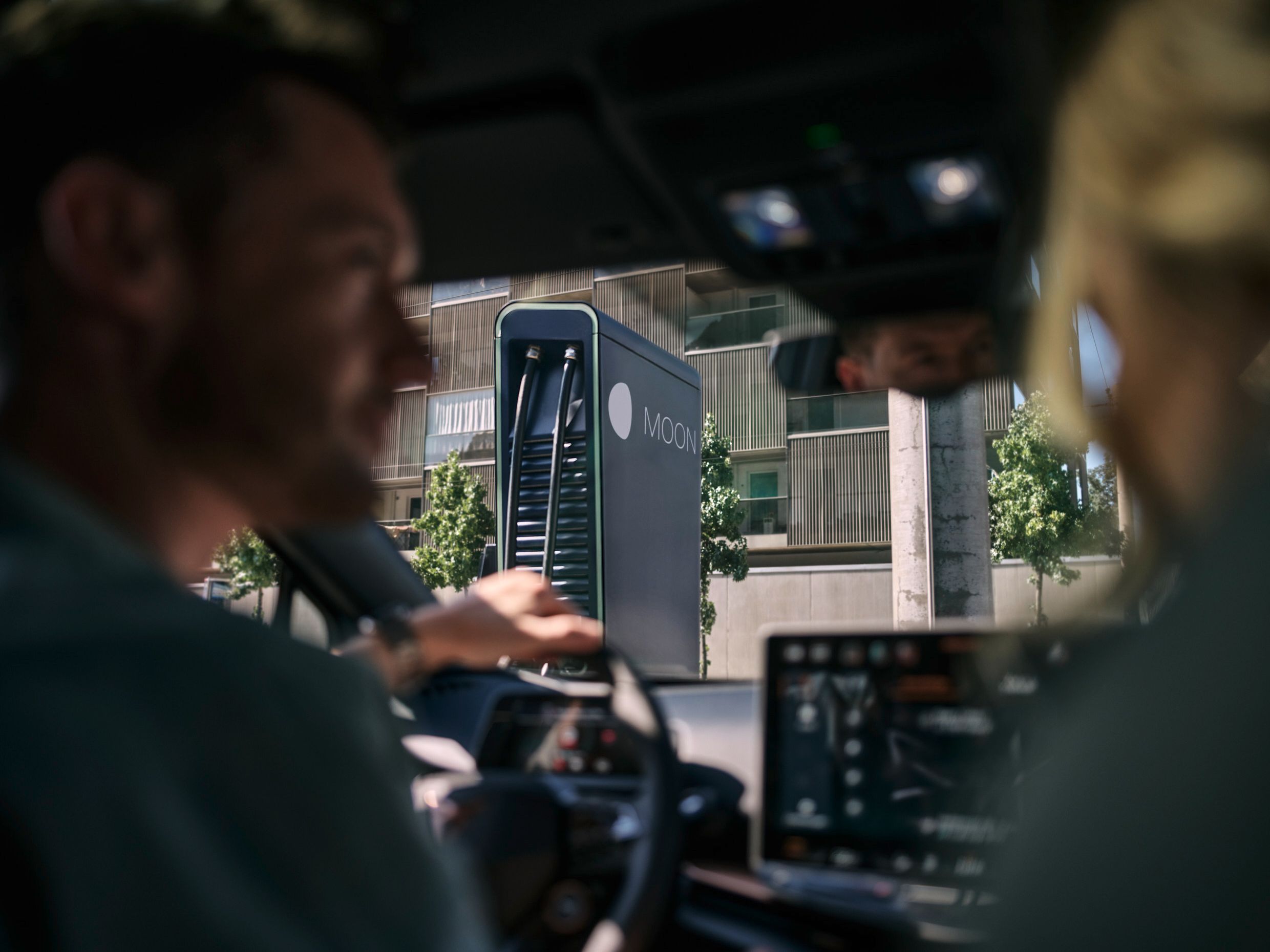 two people in a car in front of a fast charging station