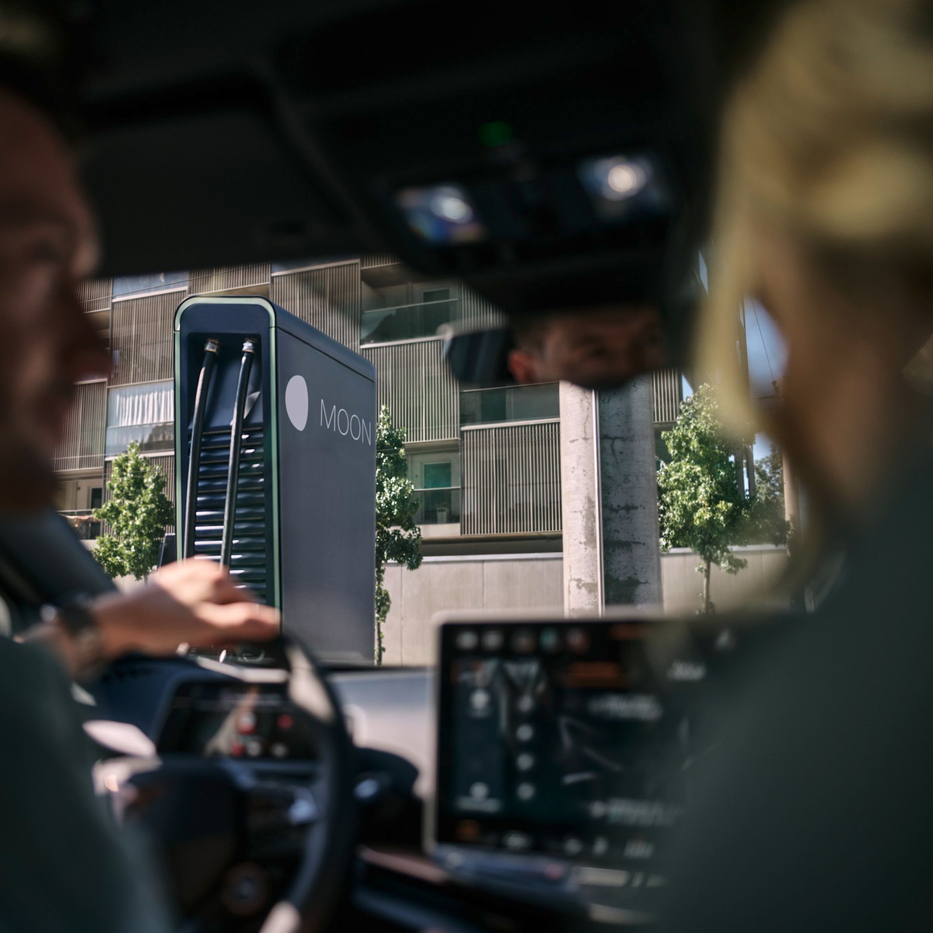two people in a car in front of a fast charging station
