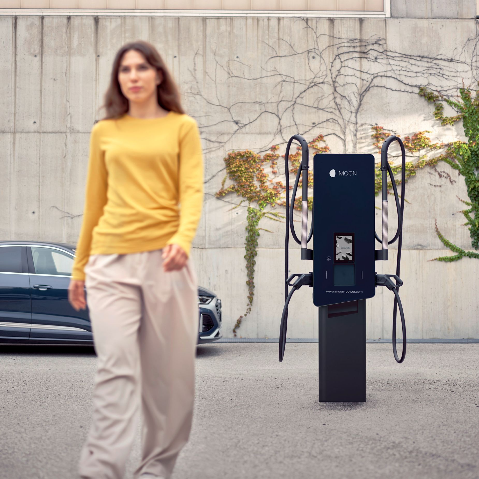 Woman walks away from a wallbox in front of an electric car