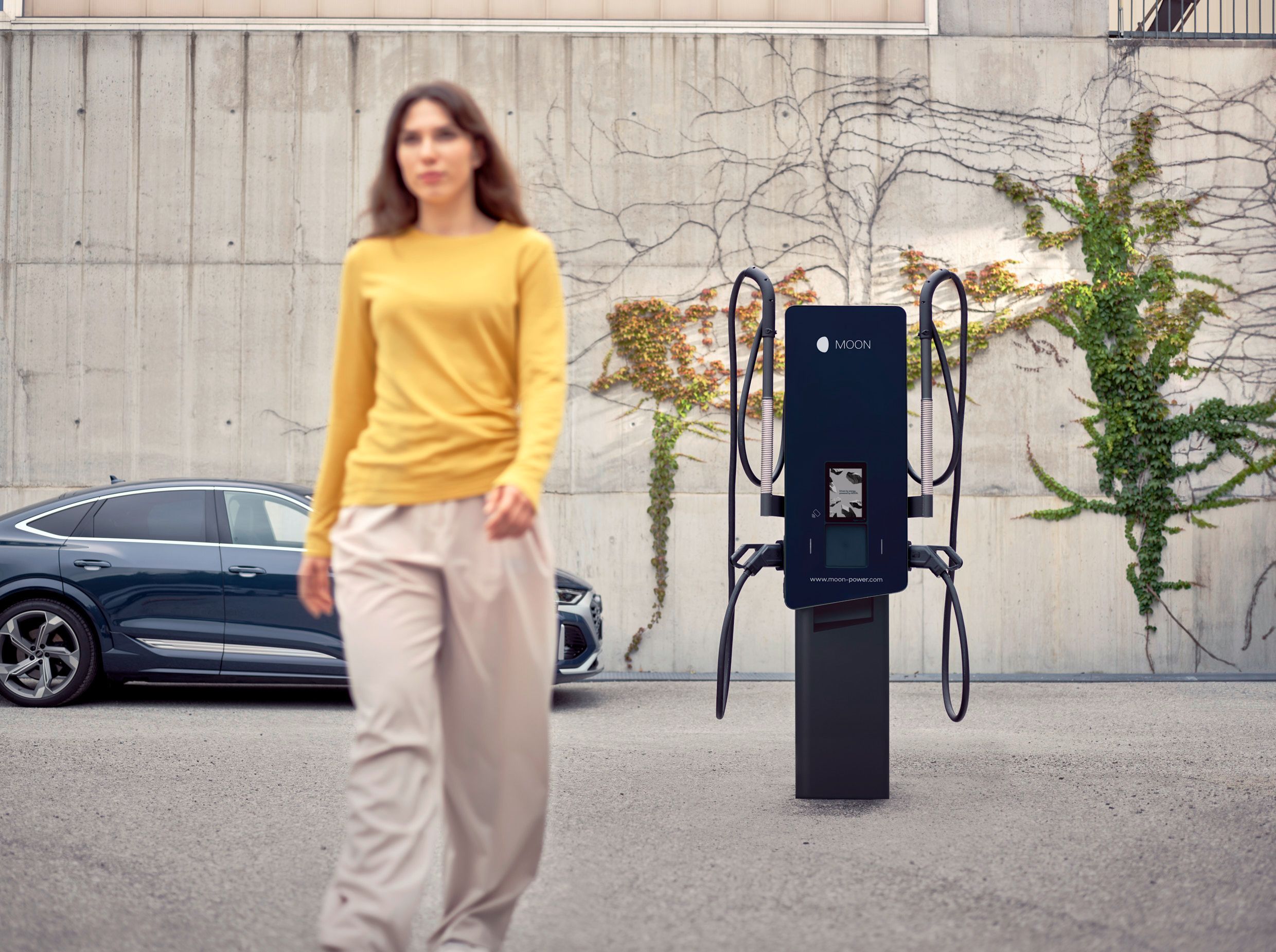 Woman walks away from a wallbox in front of an electric car