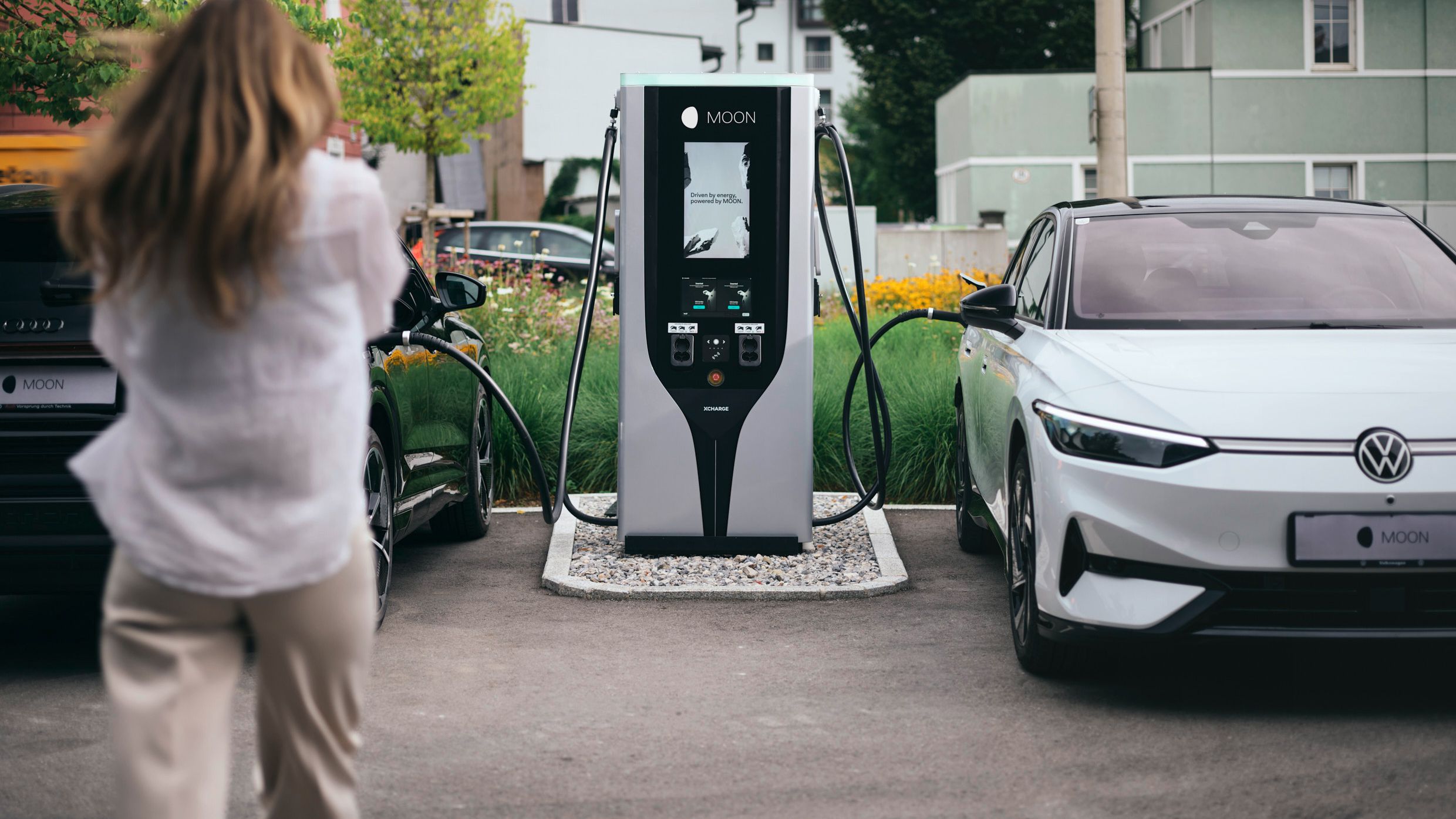 Person walks towards a fast charging station between two electric cars
