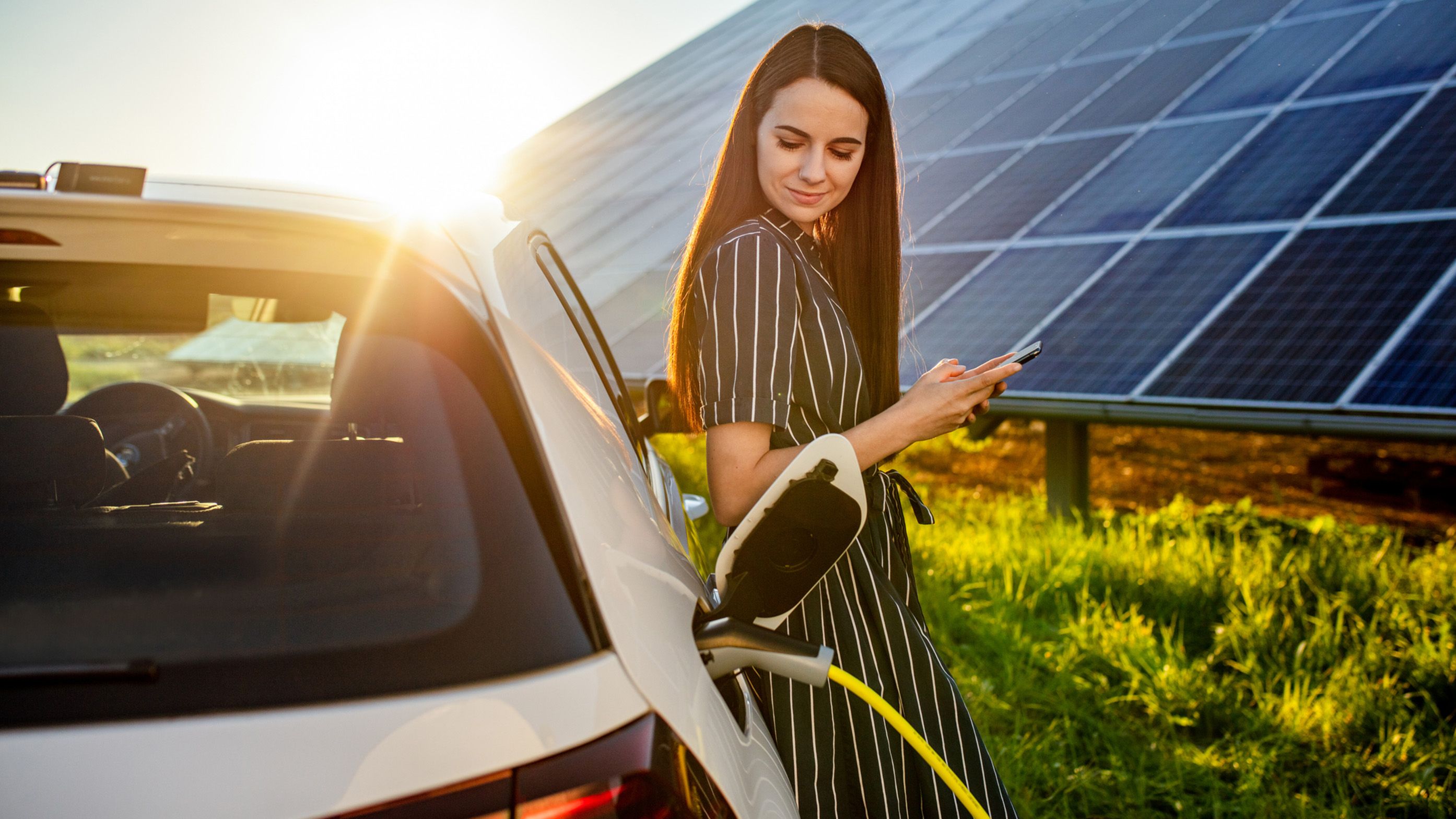 Woman leaning against a charging car in front of a photovoltaic system