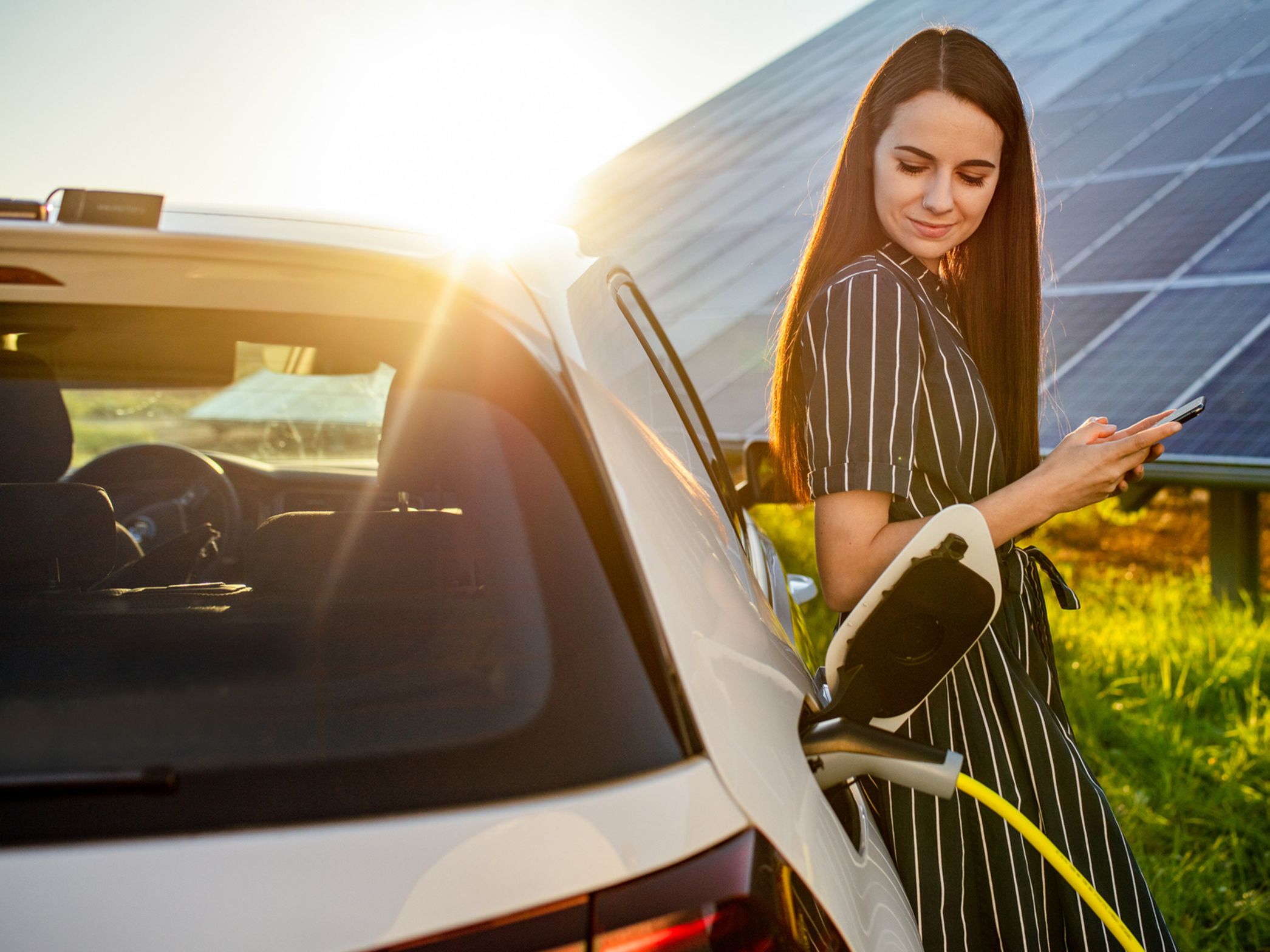 Woman leaning against a charging car in front of a photovoltaic system