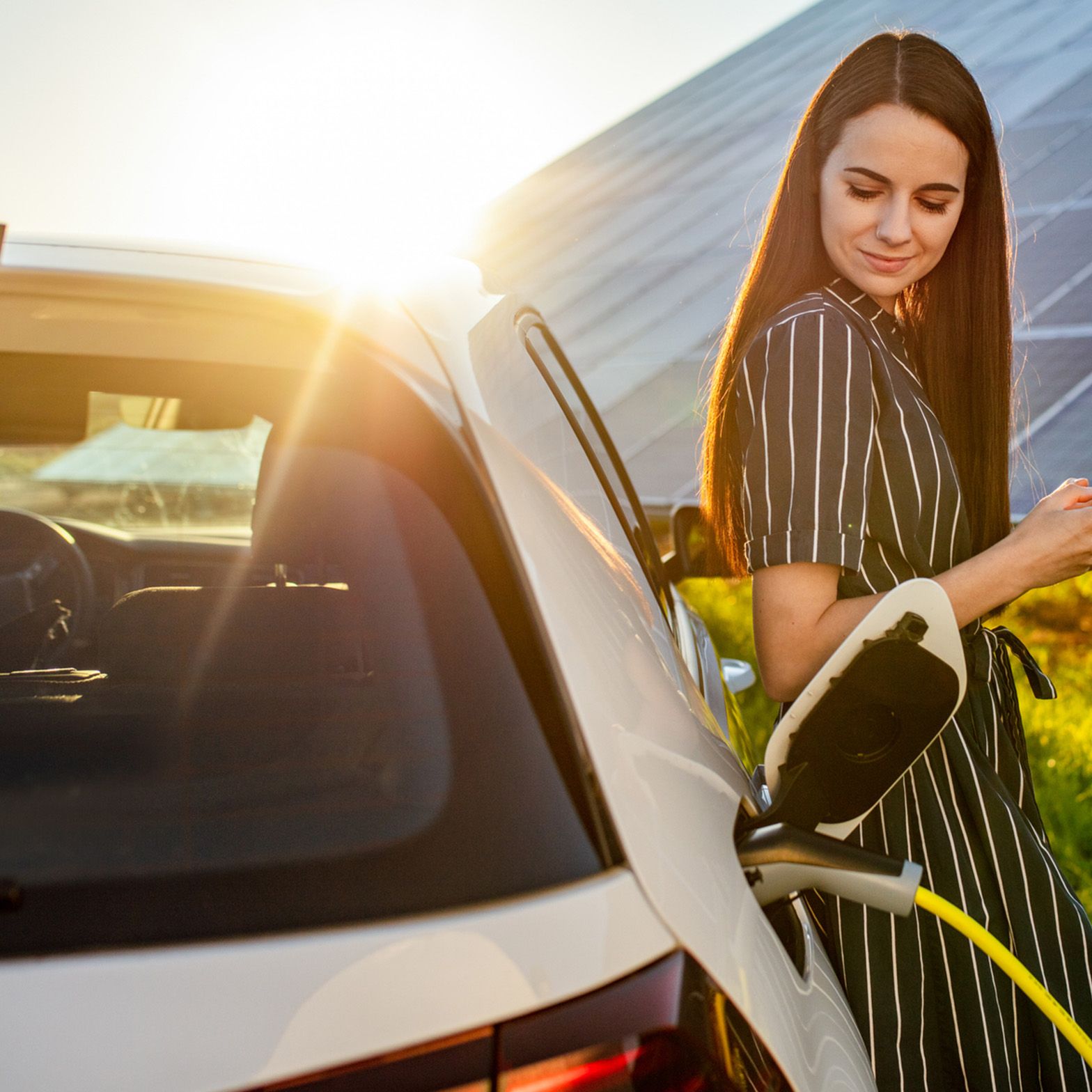 Woman leaning against a charging car in front of a photovoltaic system