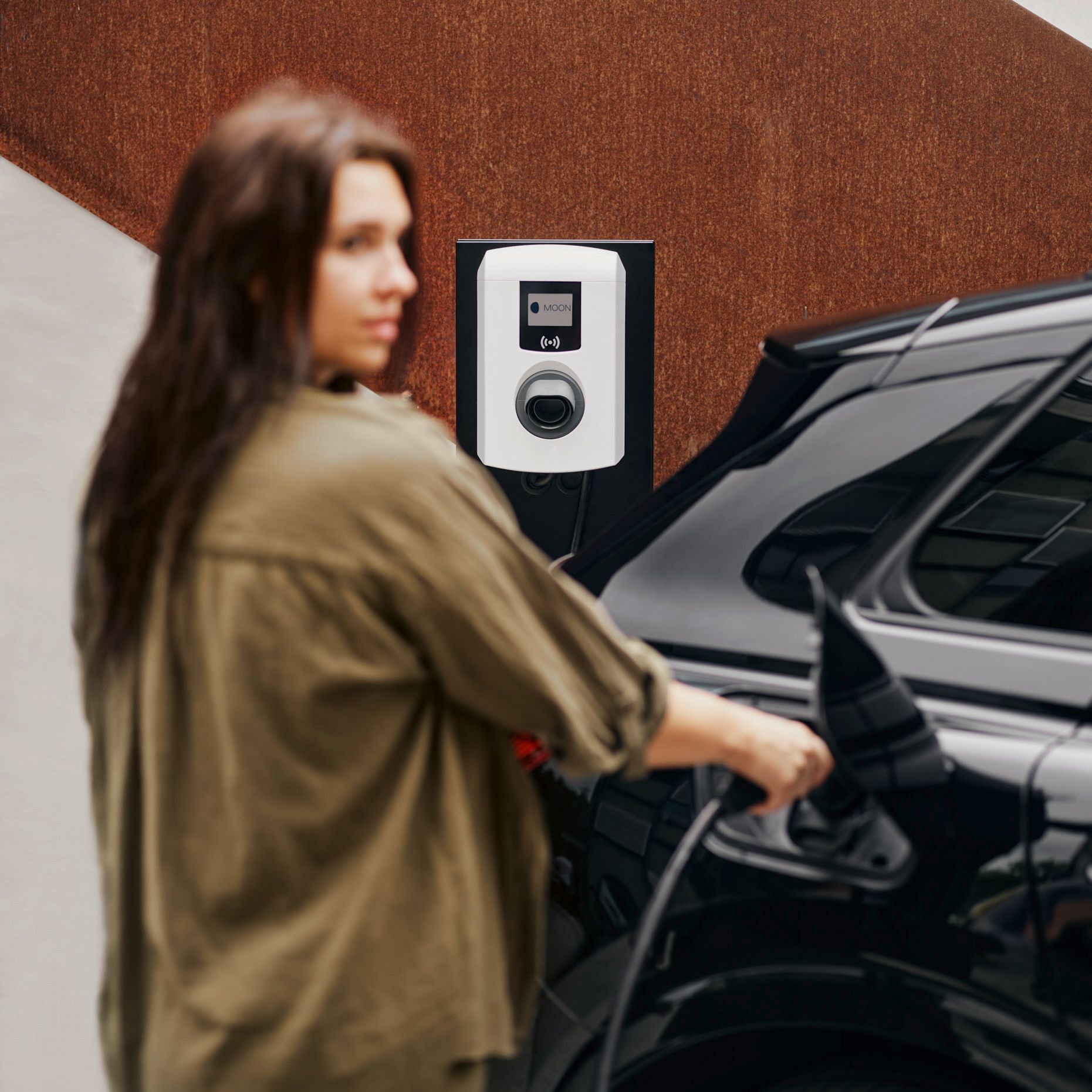 A woman puts a tap valve of a wallbox into an electric car