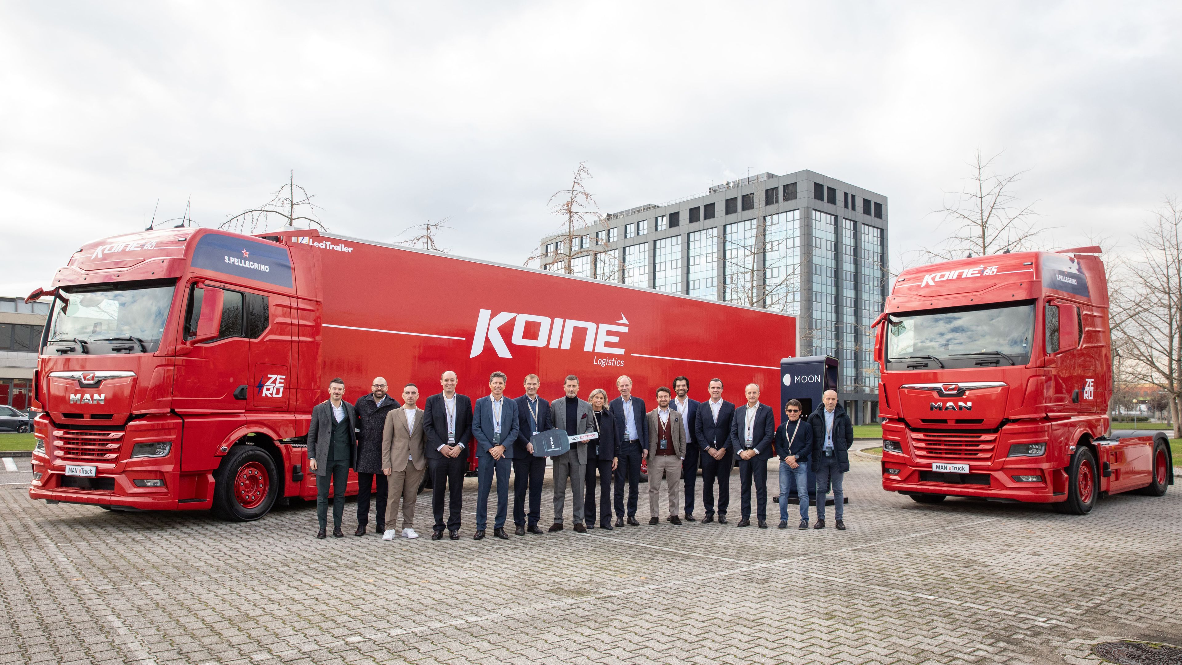 several people standing in front of two Koiné trucks in front of a POWER Charger HYC 400