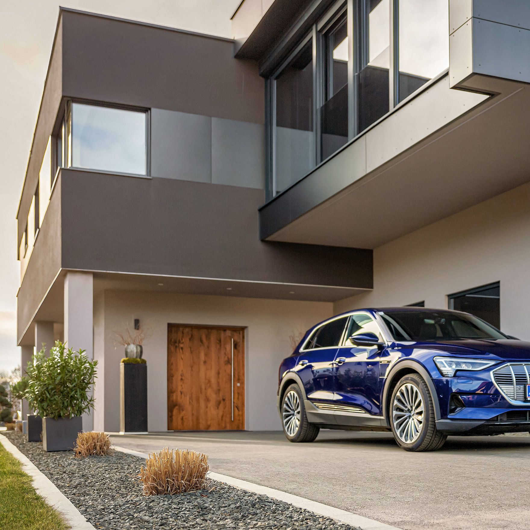 Man walks towards an electric car near a house with a cable in his hand