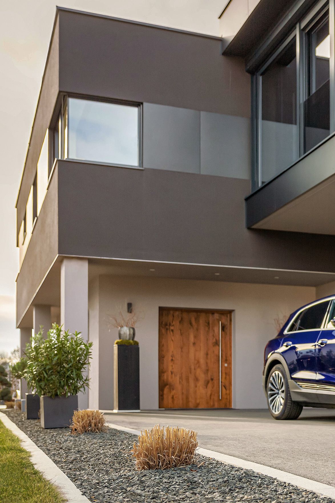 Man walks towards an electric car near a house with a cable in his hand